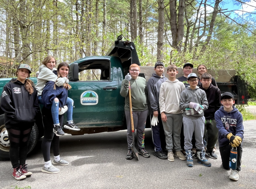 A group of middle school students stands beside a Vermont Department of Forests, Parks and Recreation truck in a wooded