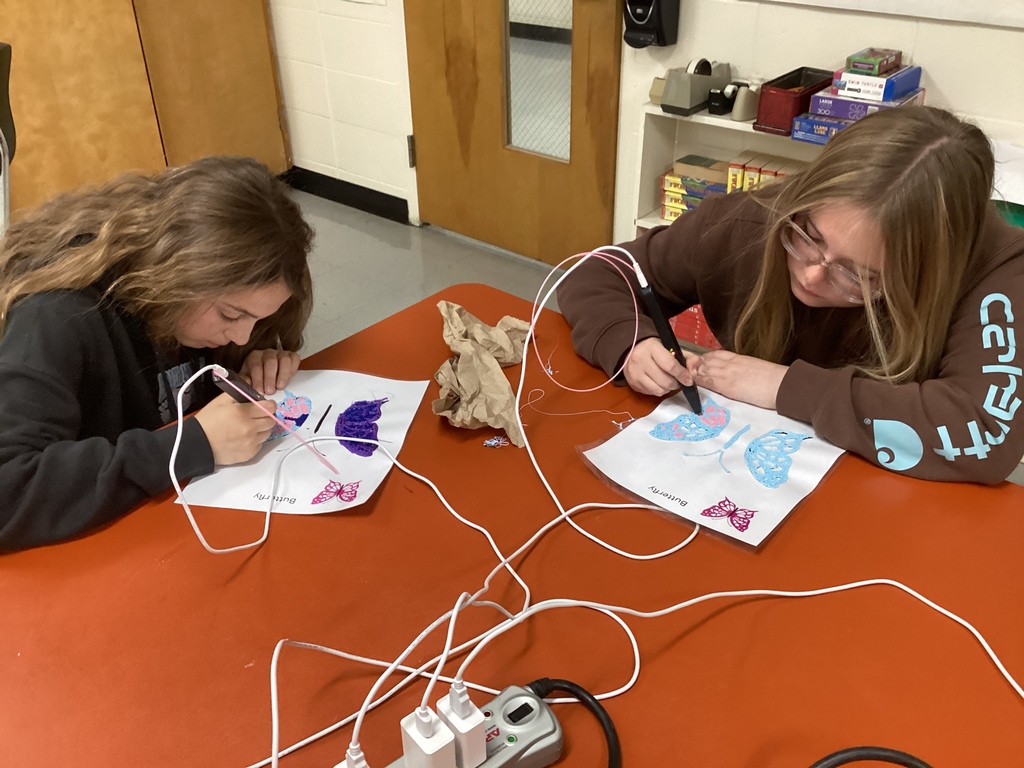 Two students use pink and white 3D pens to create colorful butterfly designs on worksheets during a library lesson about primary sources.
