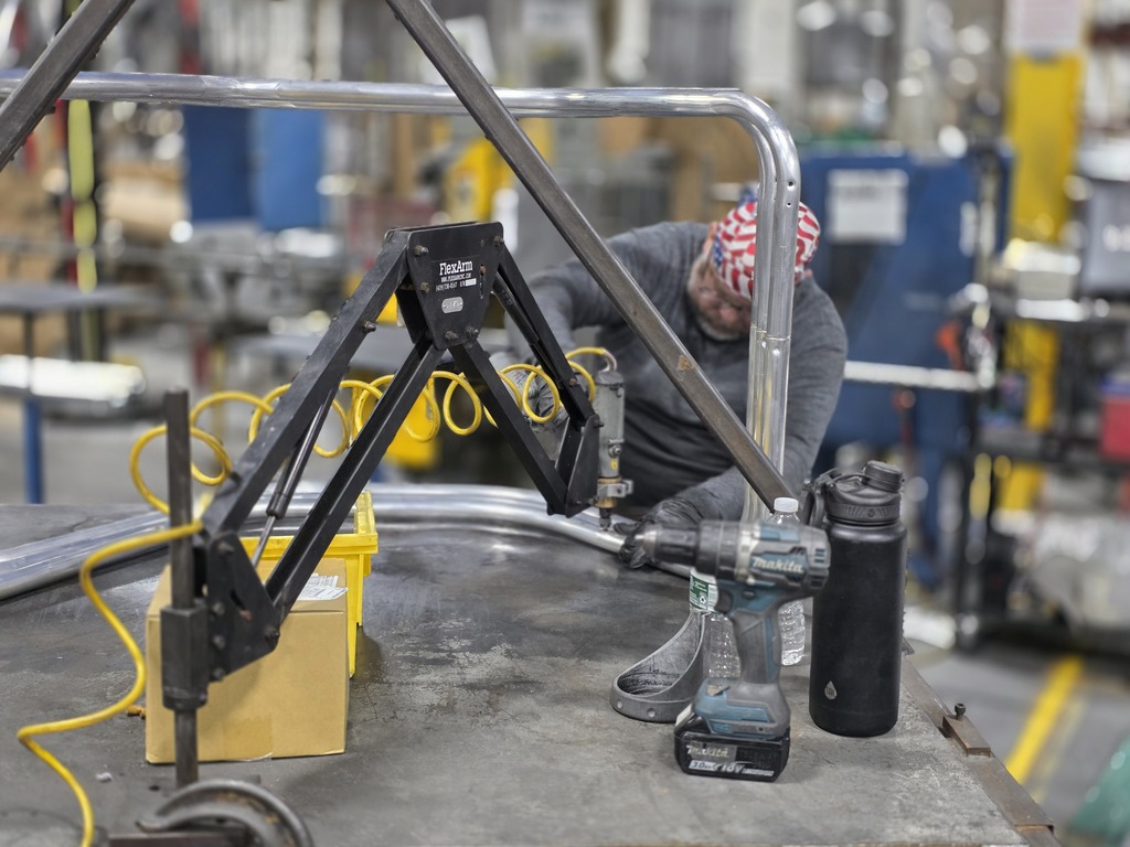 A worker wearing protective gear operates machinery on a metal worktable inside the Telescope Casual manufacturing plant. Tools and equipment are visible in the foreground.