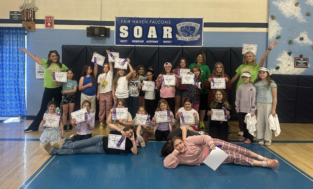 Students and staff pose together in a school gym holding certificates and award ribbons during a Fair Haven Falcons SOAR recognition celebration.