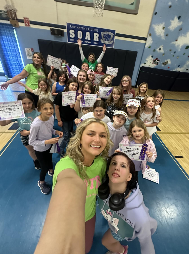 Group selfie in a school gym showing students and staff smiling and celebrating while holding certificates and purple ribbons beneath a Fair Haven Falcons SOAR banner.