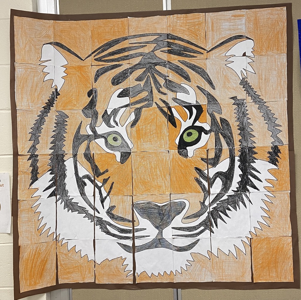 Large collaborative student mural of a tiger displayed on a wall. The artwork is created from multiple colored sections assembled together, forming a detailed tiger face with black and white markings, green eyes, and an orange-toned background.