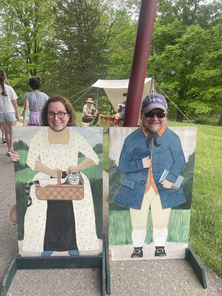 Two adults smile while posing behind painted historical character cutout boards at Mount Independence, creating a fun photo opportunity.