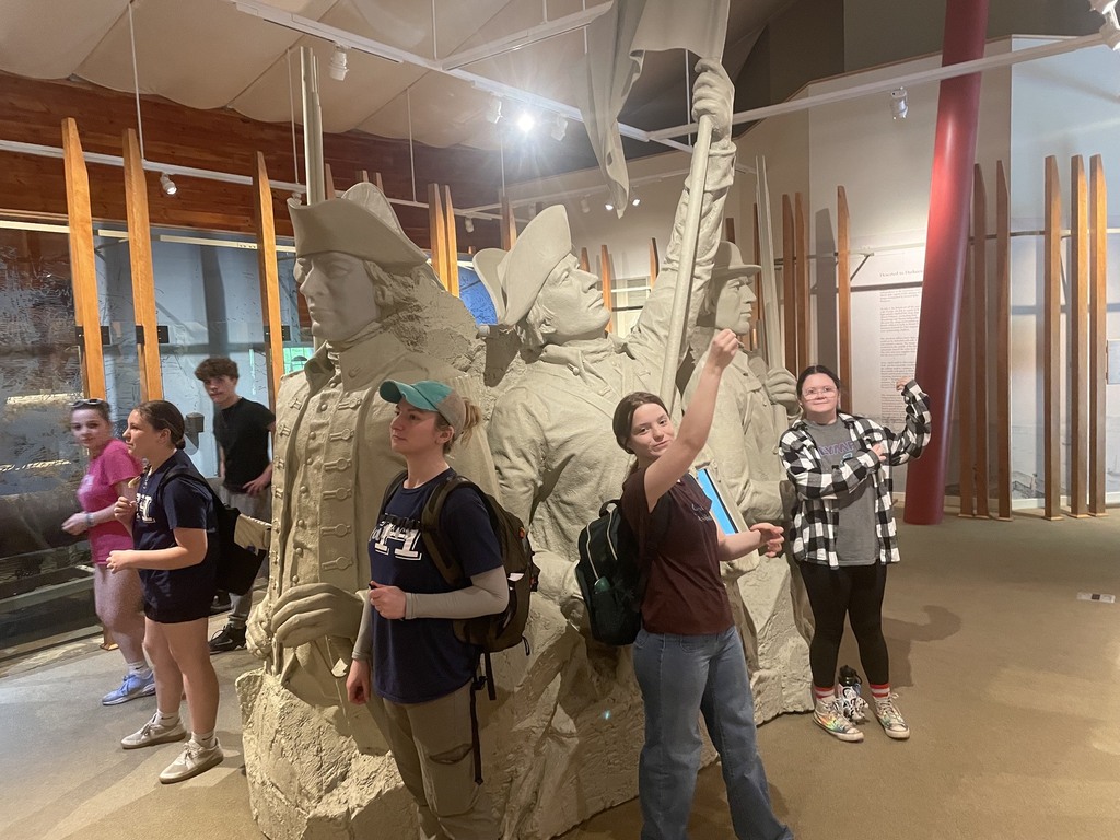 Students pose and interact around a large sculpture display of Revolutionary War figures inside a museum exhibit at Mount Independence.
