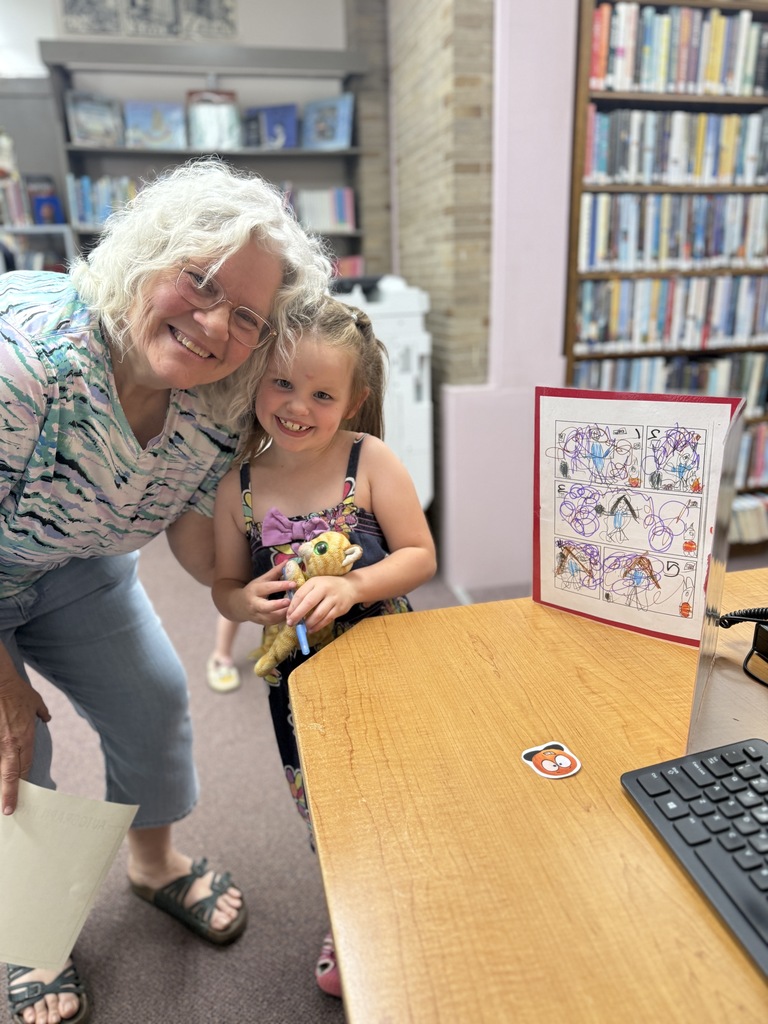A smiling family member and student pose together beside a display of the student's illustrated storybook during the book launch celebration.