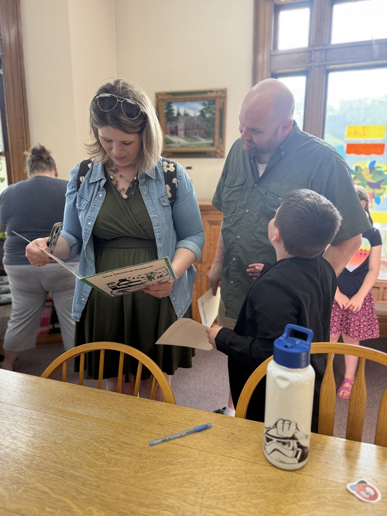 Parents and a student stand together reading and discussing a student-created book during the FHGS first grade author celebration at the Fair Haven Free Library.