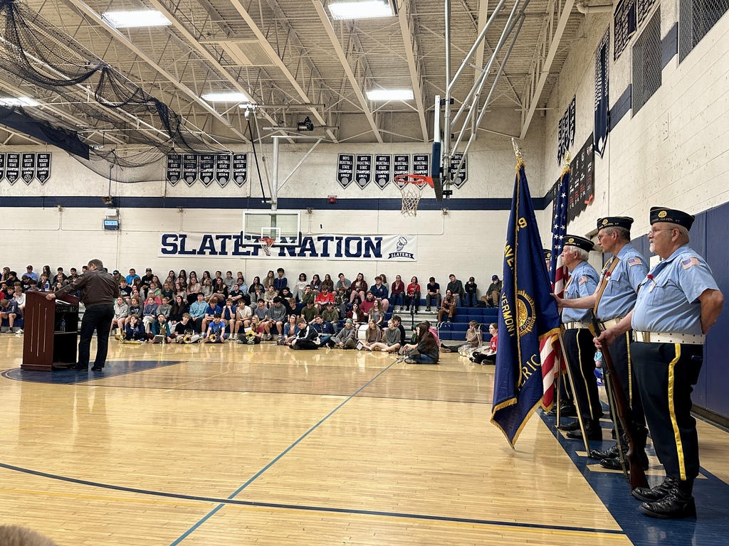 A wide view of the school gymnasium shows students gathered for the Memorial Day program while members of the Fair Haven American Legion Post 49 Color Guard stand with flags at the front.