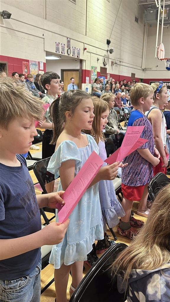 Students stand holding printed song sheets and sing together during Castleton Elementary School’s Memorial Day assembly.