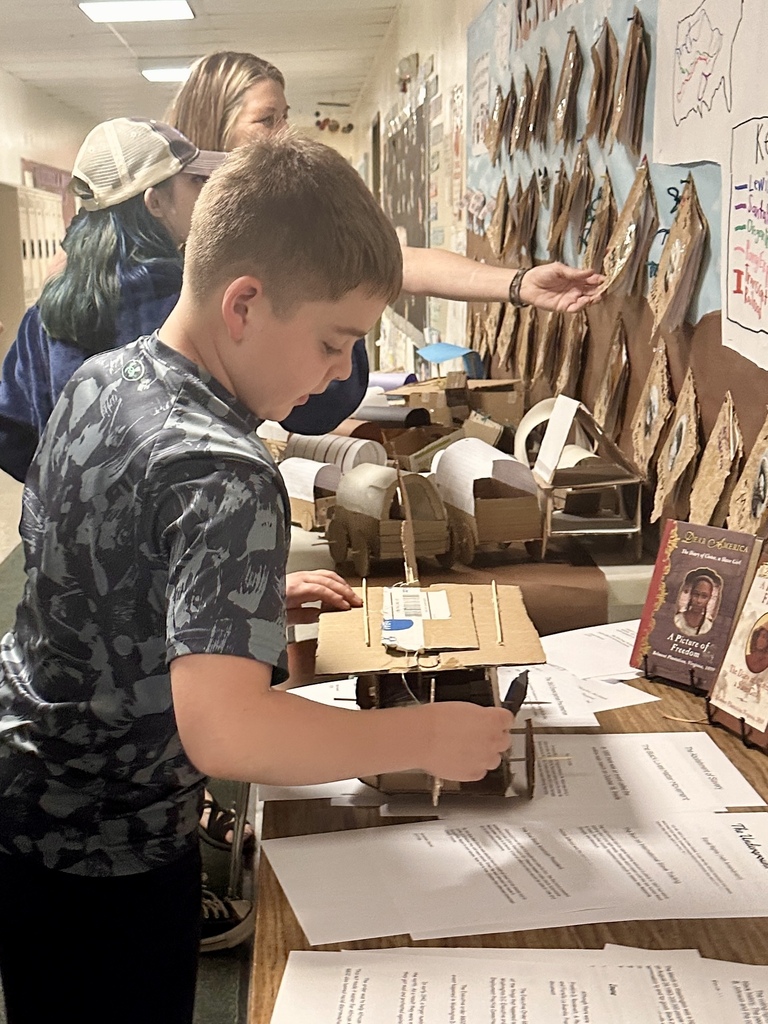 An elementary student examines a cardboard wagon model and other handmade projects displayed on a table during Castleton Elementary School’s Celebration of Learning.