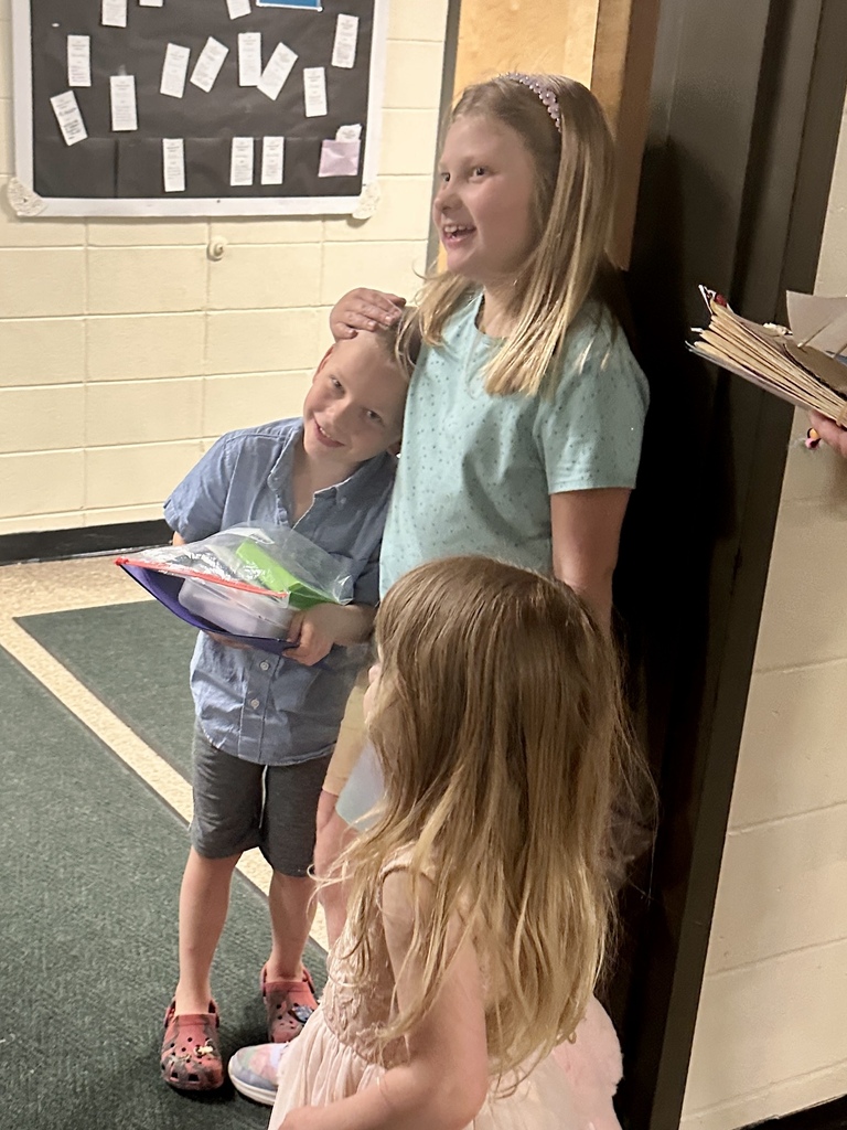 A parent and student examine a classroom display board featuring student-created projects and writing assignments mounted on brown paper.