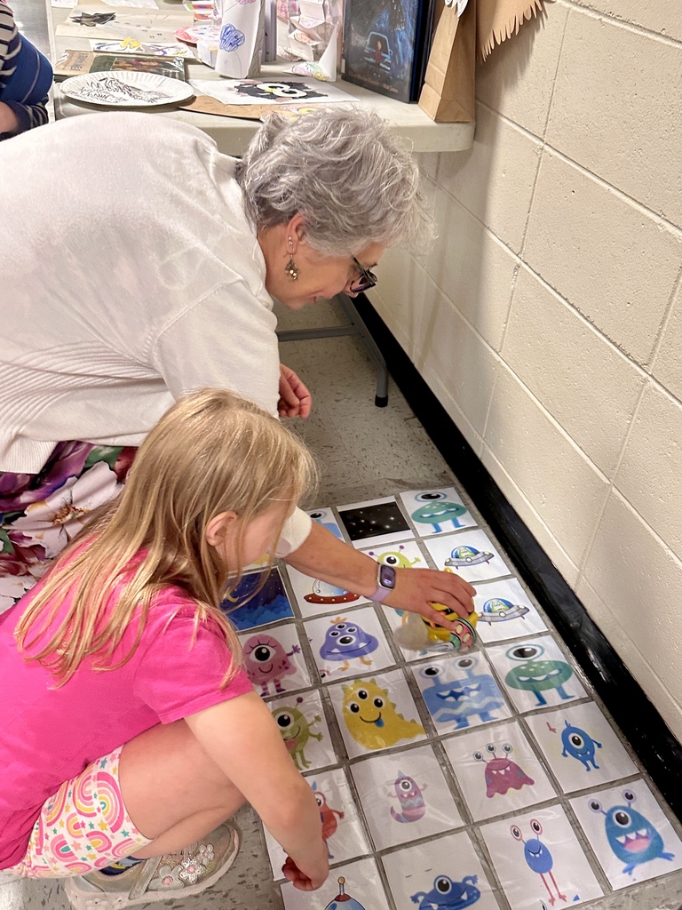 A teacher and young student kneel on the floor playing an educational matching game featuring colorful alien and spaceship cards during Castleton Elementary School’s Celebration of Learning.