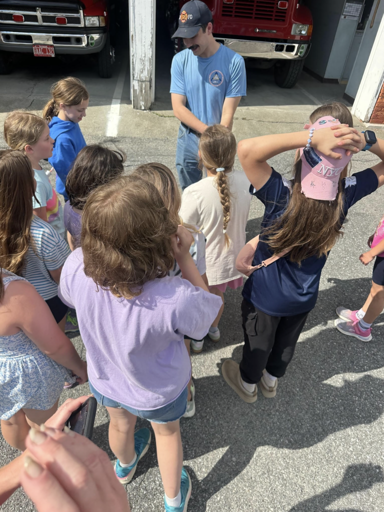 A firefighter speaks to a group of elementary students gathered outside the fire station as they learn about emergency services.