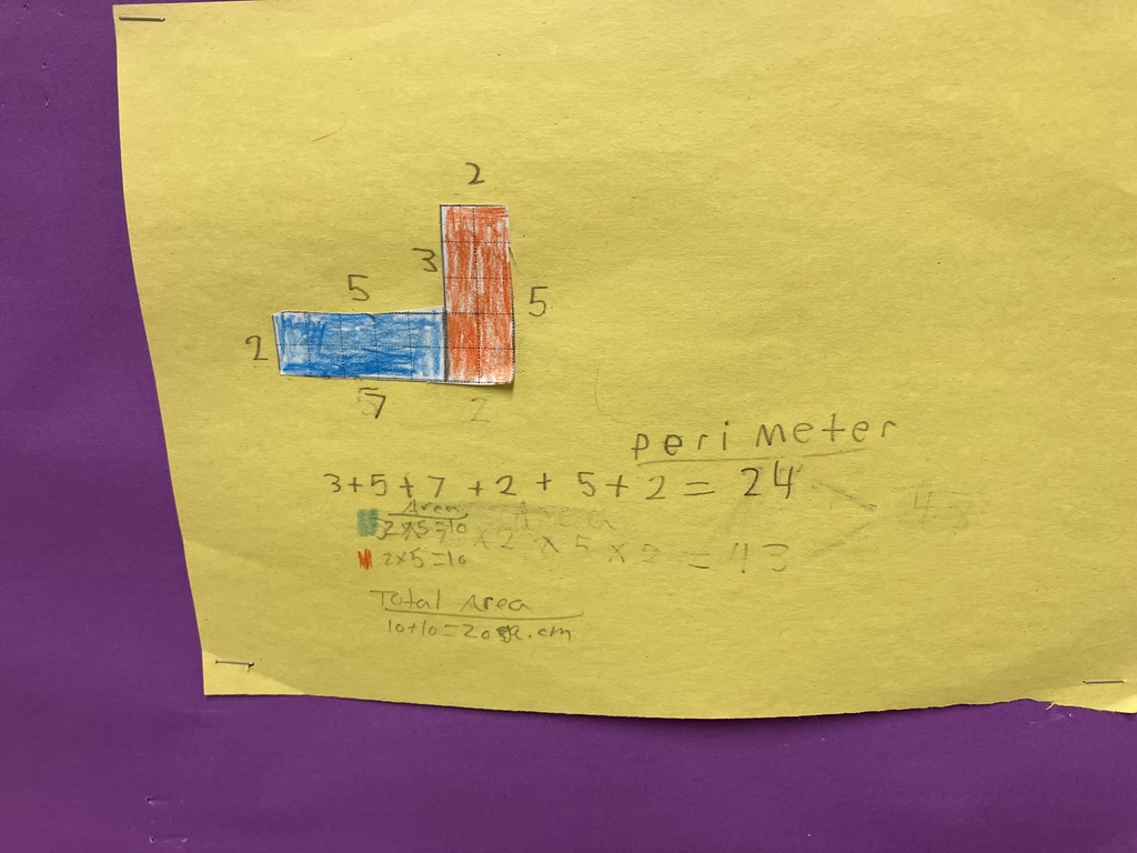  A close-up of a bright yellow piece of construction paper containing a student's math workspace. At the top, two rectangular shapes cut out of grid paper are glued together to form an asymmetrical, L-like shape; the left rectangle is colored blue and the right is orange. The dimensions are handwritten along the borders: 2, 5, 3, 2, 5, and 7. Below the shape, the student has calculated the perimeter in pencil, writing "perimeter 3 + 5 + 7 + 2 + 5 + 2 = 24." Erased and rewritten multiplication equations for area are visible underneath, concluding with "Total Area 10 + 10 = 20 sq. cm." 