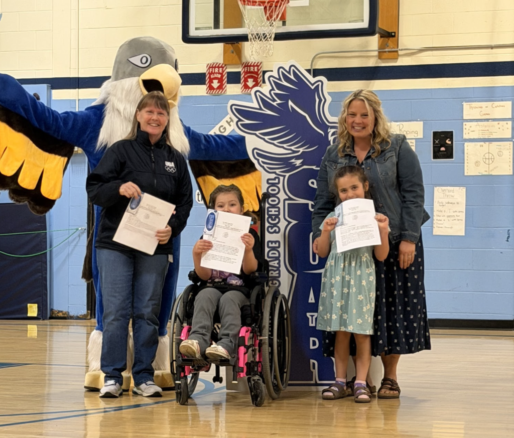 Two young students holding certificates pose with two adults and the Falcon mascot during a student recognition assembly at Fair Haven Grade School.