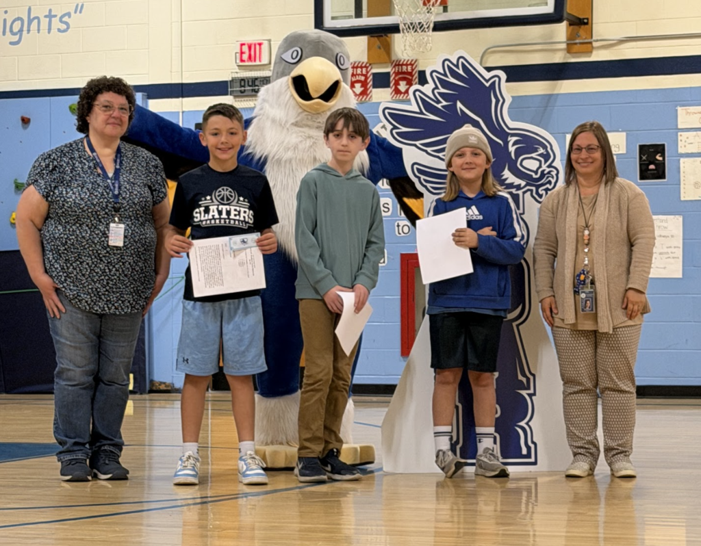 Three students stand with two staff members and the Falcon mascot during an awards presentation at Fair Haven Grade School. One student holds a recognition certificate.