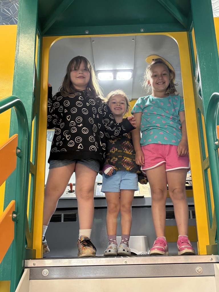 Three smiling students stand together in the doorway of a train exhibit, posing for a photo inside the museum.