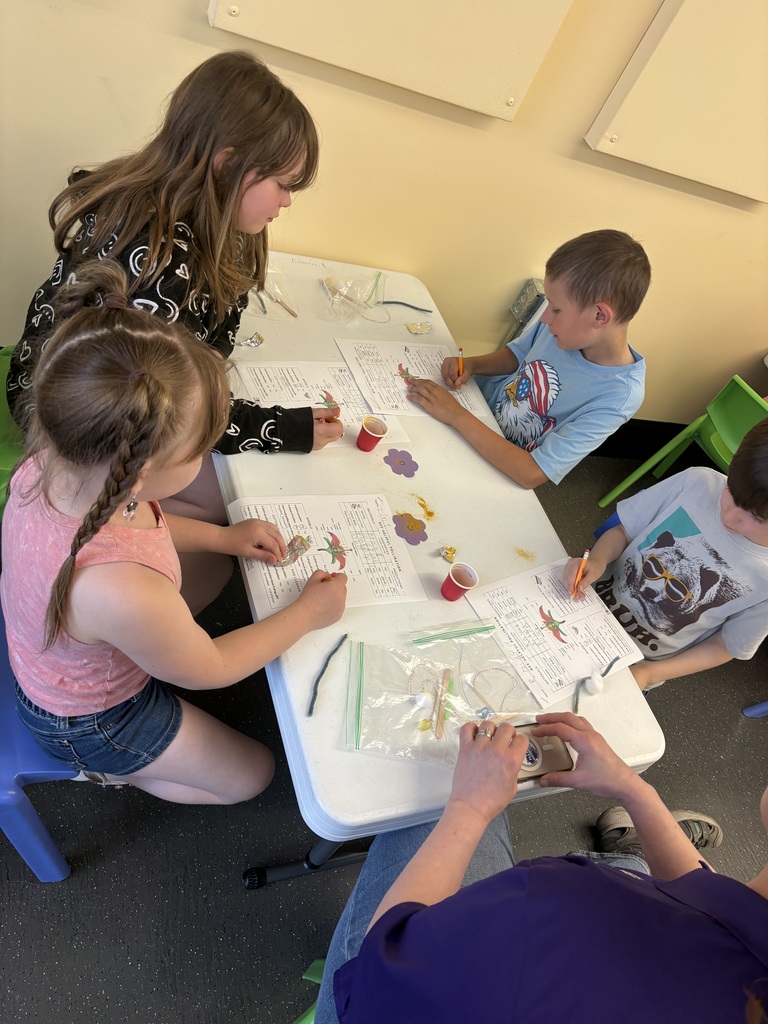 A group of students gathers around a table, designing and testing hand pollinators with various materials while completing a lesson about bees and pollination.