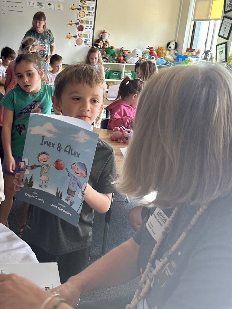 A student proudly holds up a signed copy of Inex & Alex while speaking with Mrs. Kristen Ramey during the book-signing session.