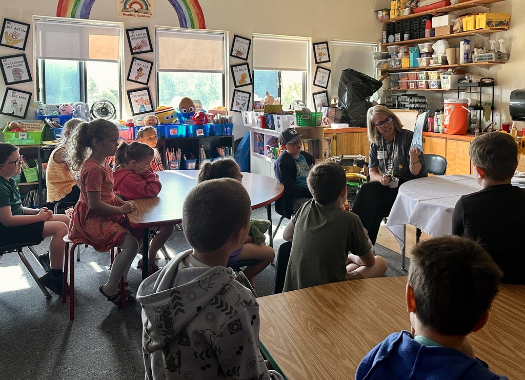 Mrs. Kristen Ramey reads Inex & Alex to a classroom of first-grade students seated around tables and listening attentively.