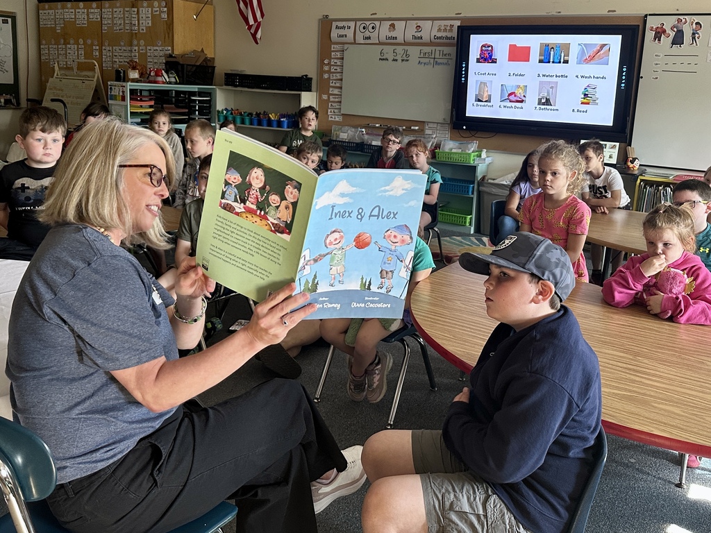 Mrs. Kristen Ramey reads Inex & Alex to a group of first graders gathered around her in their classroom.