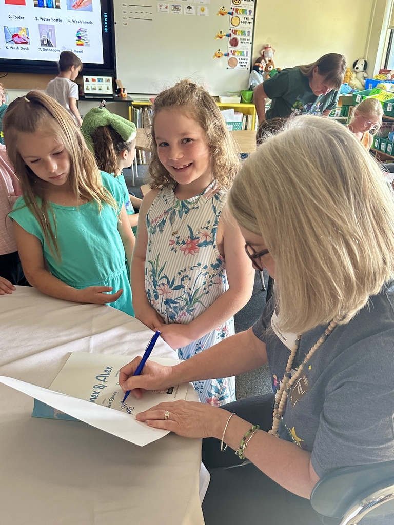 Mrs. Kristen Ramey signs a copy of Inex & Alex while two smiling students wait nearby to receive their books.