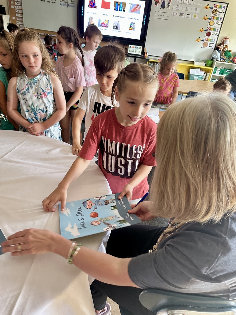 A student presents a copy of Inex & Alex to Mrs. Kristen Ramey as she signs books for the class.