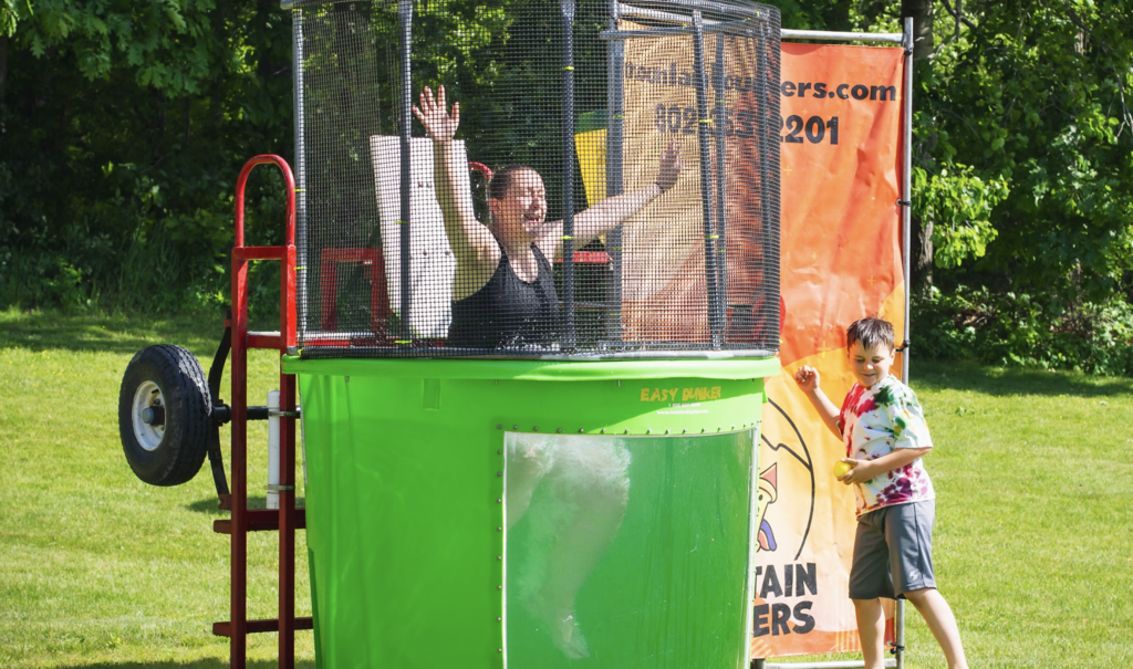 A staff member sits in a dunk tank with arms raised while a student prepares to throw a ball at the target during the Big Celebration.