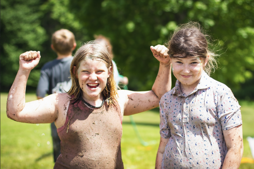 Two students covered in mud and grass smile and flex their arms after participating in messy outdoor activities during the Big Celebration.