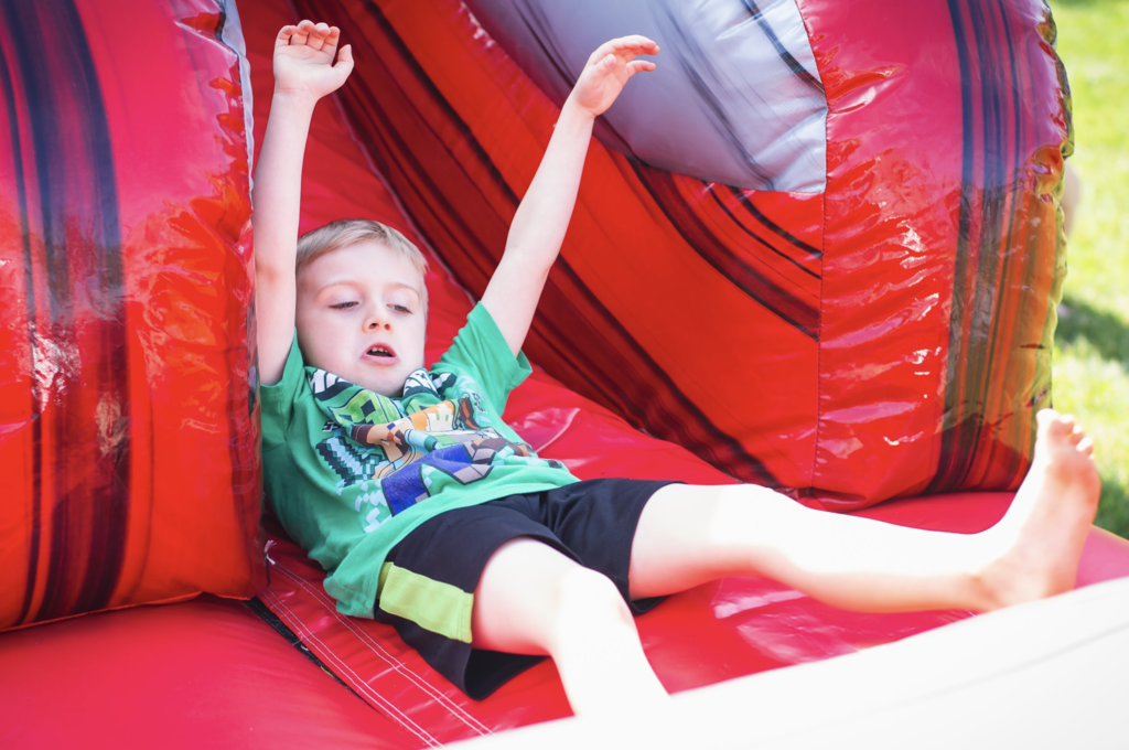 A young student raises both arms while sliding down a bright red inflatable bounce house slide during the celebration.