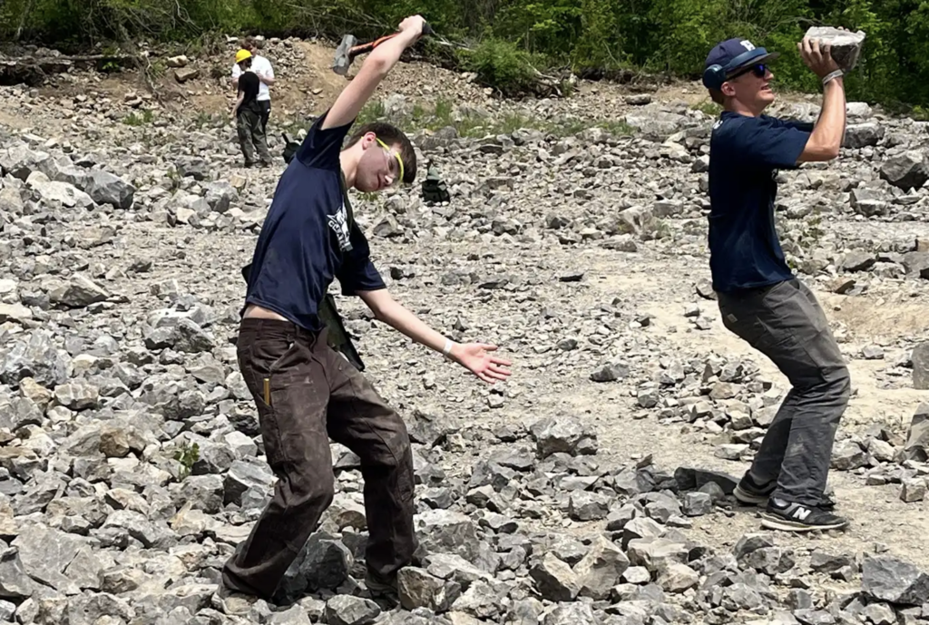 Two students pose playfully in the quarry. One dramatically swings a rock hammer while another pretends to lift a large rock, mimicking scenes from the video game Minecraft.