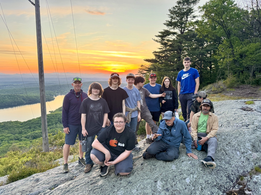 Students and teacher chaperones gather on a rocky overlook above Silver Lake at sunset, with mountains and colorful evening skies in the background.