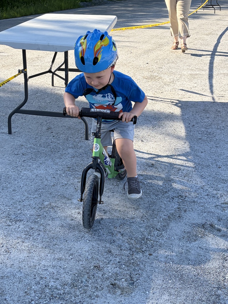 A wide shot of the school's "Bike and Groove" event. Dozens of students are riding their bicycles along a paved path winding through the school campus, surrounded by green grass [and trees/school buildings].