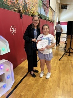 Student proudly displays a certificate while standing beside a staff member in the gym.