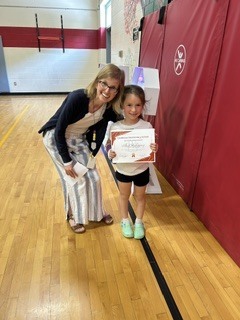 Student proudly holds a certificate while posing with a staff member during an awards ceremony.
