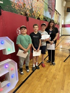 Three students and a staff member pose together with certificates during a school awards presentation.