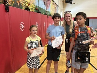 Three students recognized for their achievements stand together holding certificates with a staff member.