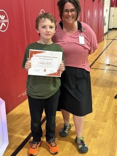 A student proudly holds a certificate while standing with a staff member in the gym.