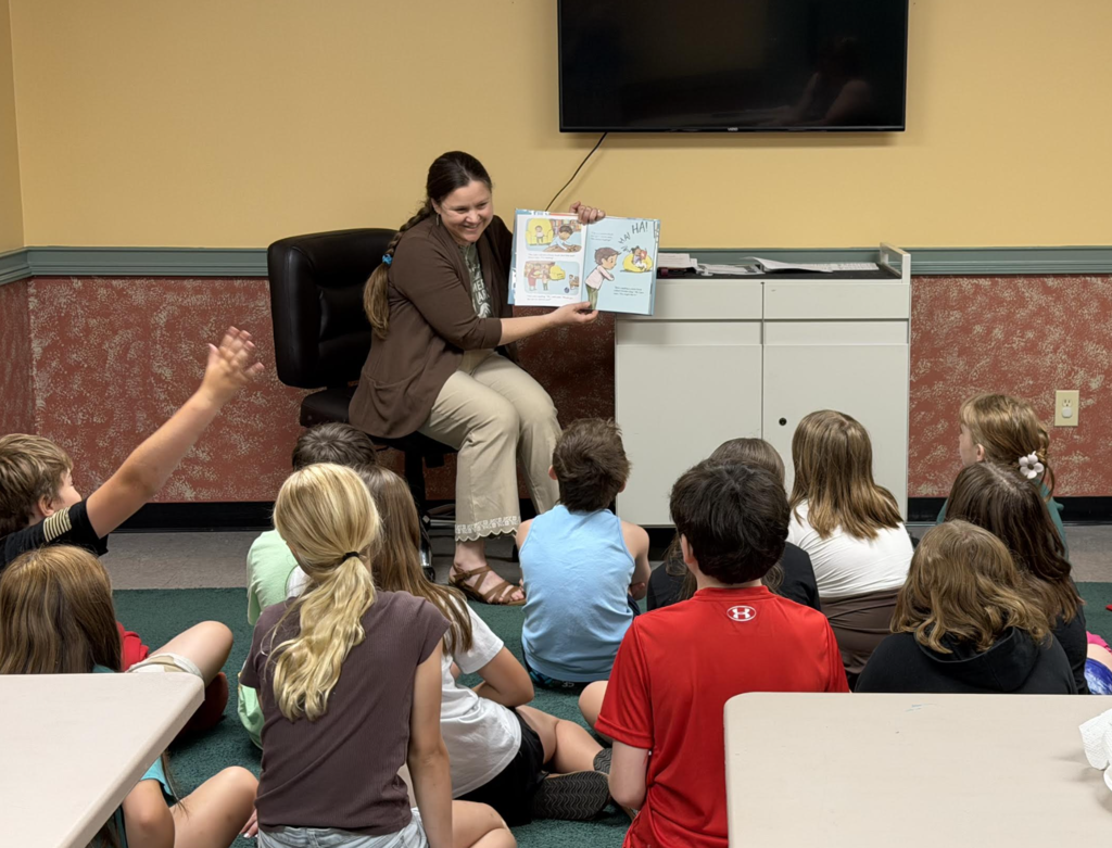 A librarian smiles while sharing a picture book with attentive fourth-grade students gathered for story time at the Fair Haven Public Library.