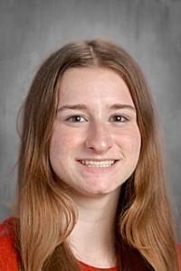 School portrait of a student with long, light brown hair smiling at the camera. The student is wearing a red top and is photographed against a gray studio background.