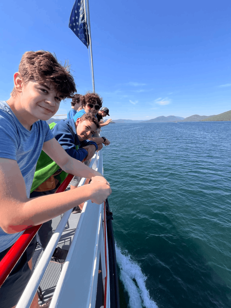 Students lean over the railing of a boat, taking in views of Lake George and the surrounding Adirondack Mountains.