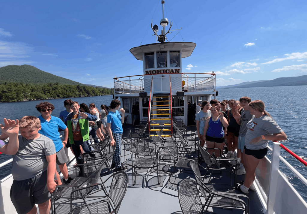 Students enjoy the sunshine on the upper deck of the Mohican boat while cruising across Lake George.