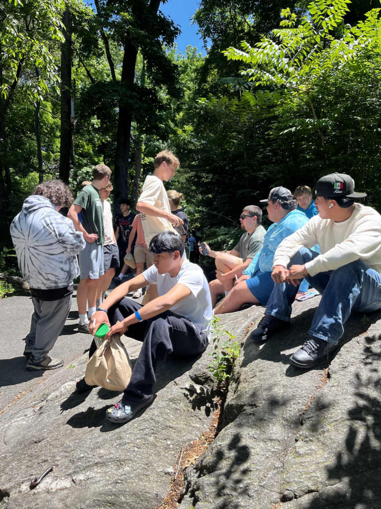 Several students relax on large rocks and along a pathway at the Bronx Zoo while enjoying the sunny weather and spending time together before heading home.