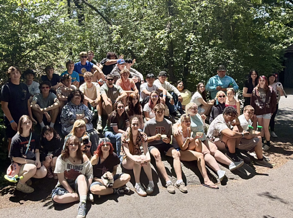 Group photo of Fair Haven Union High School seniors gathered outdoors on large rocks and pathways at the Bronx Zoo, smiling together in the shade of tall trees.