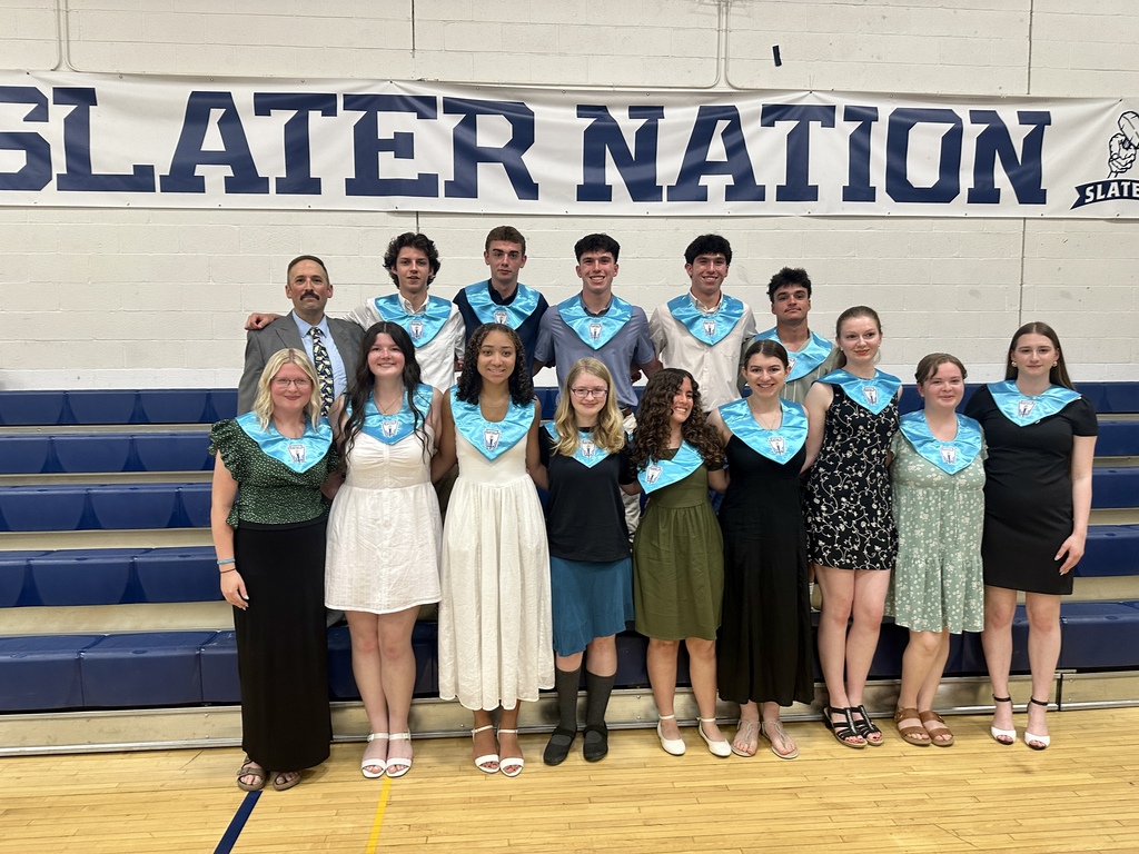 Group portrait of the Matthew Lyon Chapter National Honor Society members and new inductees standing in front of the bleachers beneath a large “Slater Nation” banner in the Fair Haven Union High School gymnasium. Students wear formal attire and NHS stoles alongside NHS Advisor Mr. Bruce.