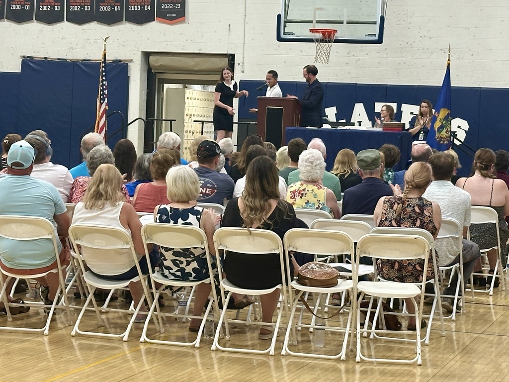 A student receives an award on stage during the Scholarship and Honor Awards Ceremony while audience members applaud. The gymnasium is filled with students, families, and community members gathered to celebrate student achievements and scholarships.