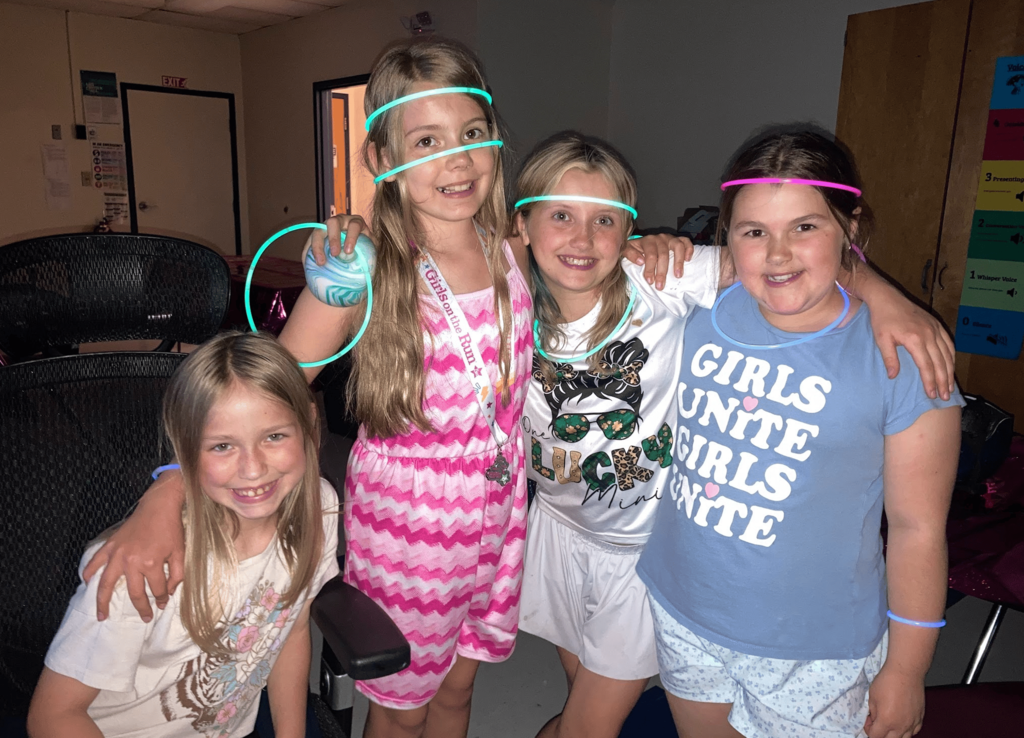 Four Girls on the Run participants wearing glow necklaces and bracelets smile together during the glow dance party.