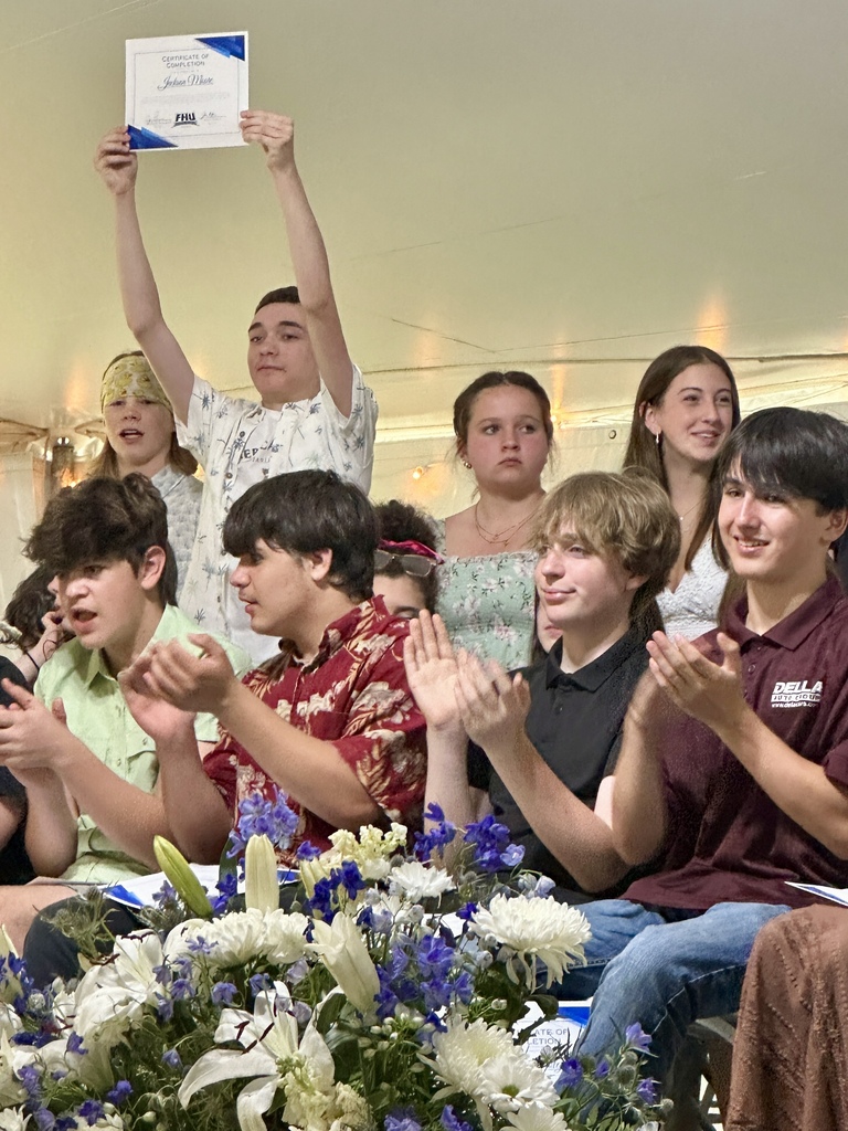 Students applaud as a classmate proudly raises a certificate above his head during the celebration ceremony.