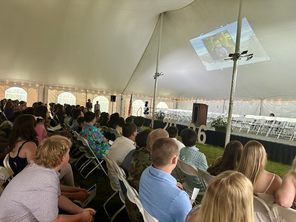 Families and students sit under a large tent watching a slideshow projected onto the ceiling during the eighth-grade celebration.