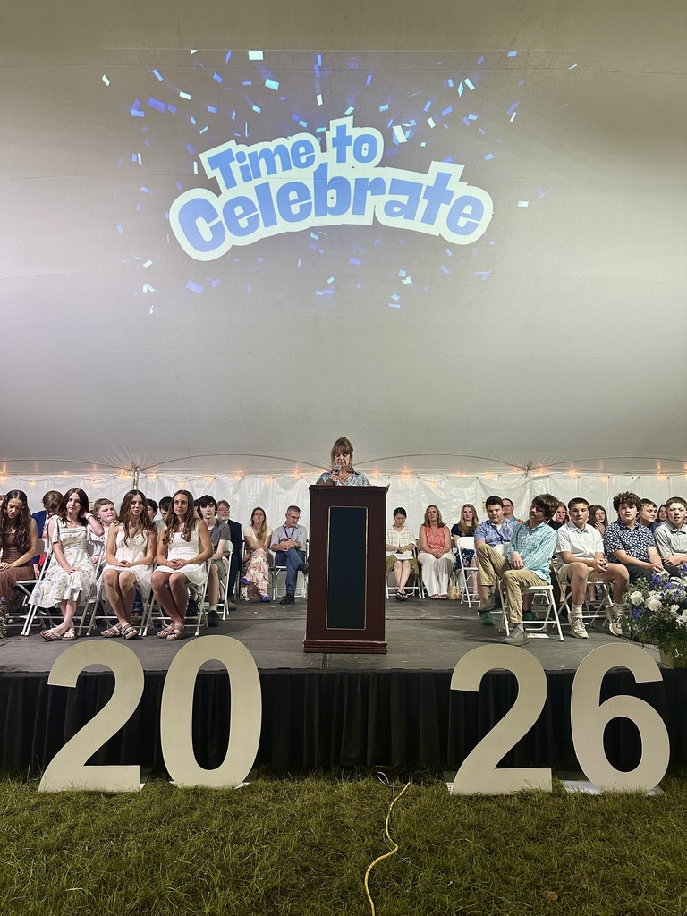Students sit on stage behind a podium during the Fair Haven Union Middle School Eighth Grade Celebration. A "Time to Celebrate" graphic is projected on the tent wall above large white numbers reading 2026.