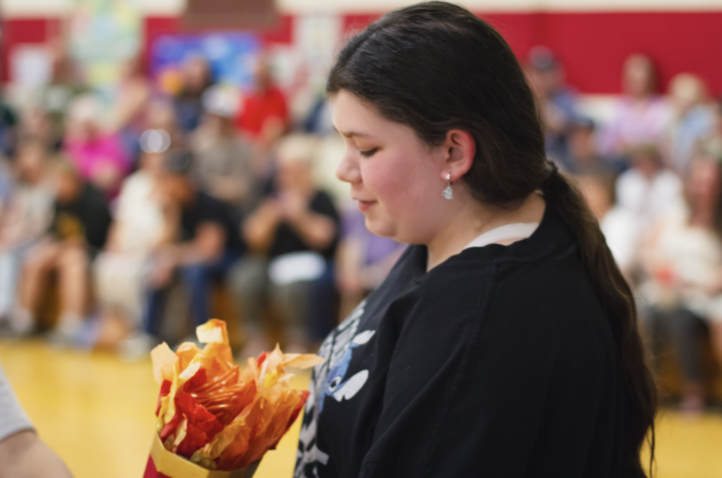 A sixth-grade student holds the ceremonial torch while standing in front of families and community members gathered for the event.